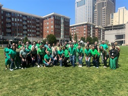 Photo of a group of people wearing green standing at a greenspace park. 