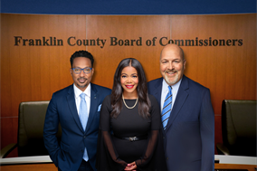3 County Commissioners standing infront of the board of commissioners' hearing room