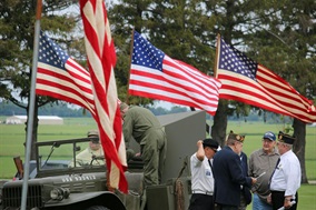Several American flags atop an Army Jeep with three veterans standing behind it chatting