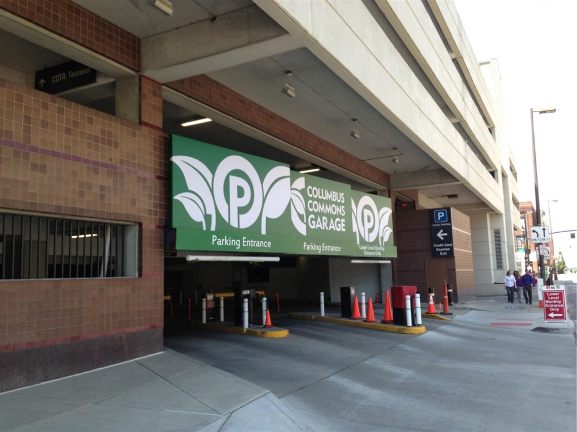 Entrance to the Columbus Commons Garage parking facility with multiple vehicle entry lanes, parking signs, and a downtown sidewalk alongside the garage.